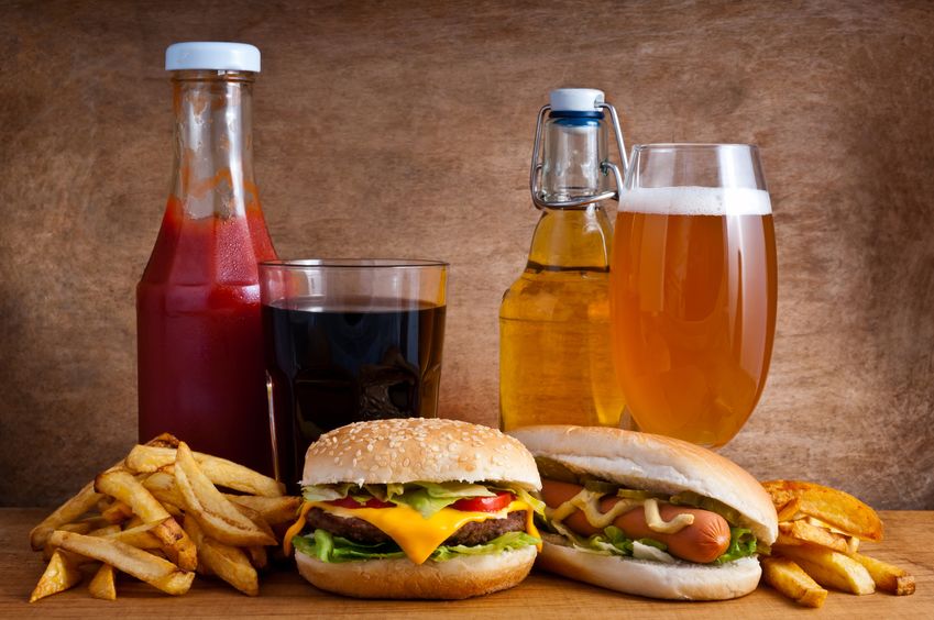 Junk food with burger, hotdog, french fries, cola, ketchup and beer on a wooden background