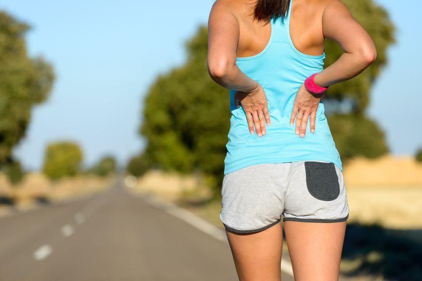 Woman suffering from painful lumbago while running in rural road.