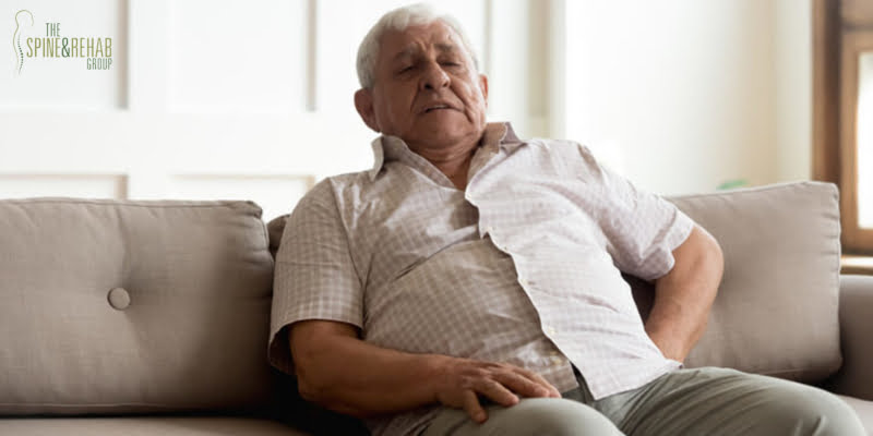 an older man sitting on the couch and holding his back in pain